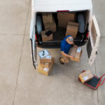 Delivery man holding cardboard box and unloading parcel for delivery. Top view of courier unloading parcels from van. High angle view of man removing packages for the delivery.
